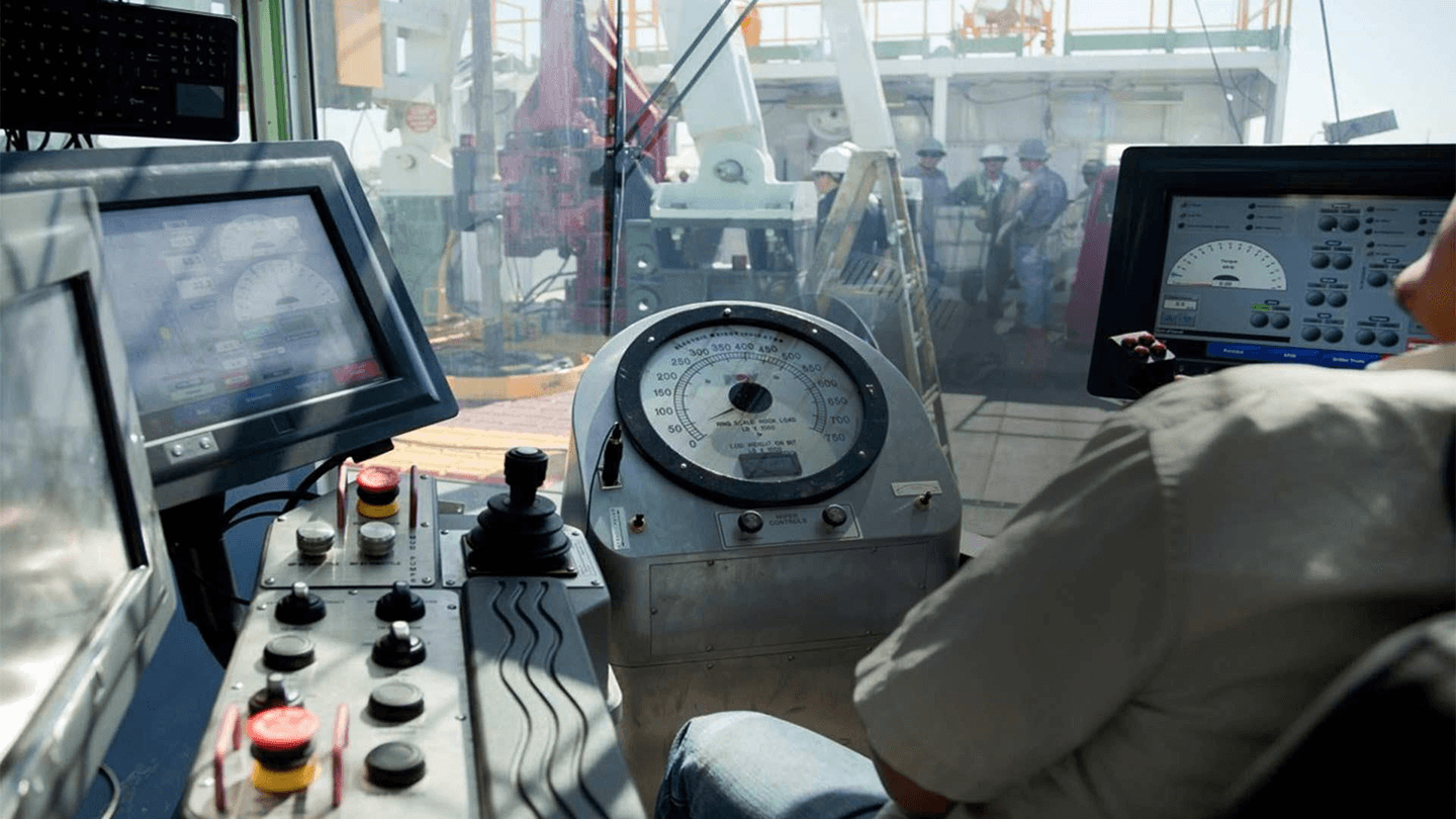 A driller's cabin crowded with screens, gauges and controls above the rig floor